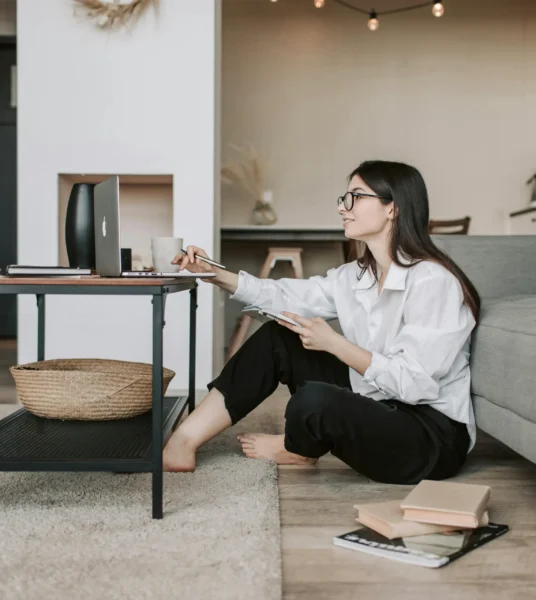 Woman working from home, sitting on the floor with a notebook and laptop.