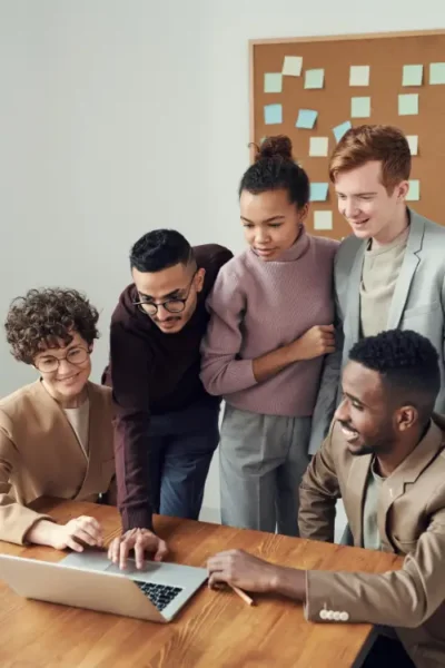 Group of diverse colleagues gathered around a laptop, collaborating on a project.