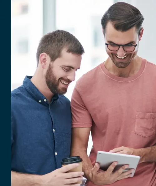 Two men smiling and looking at a tablet together in a professional setting.